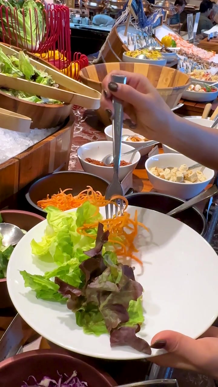 Close-up shot of a person selecting shredded carrots and lettuce at a restaurant buffet