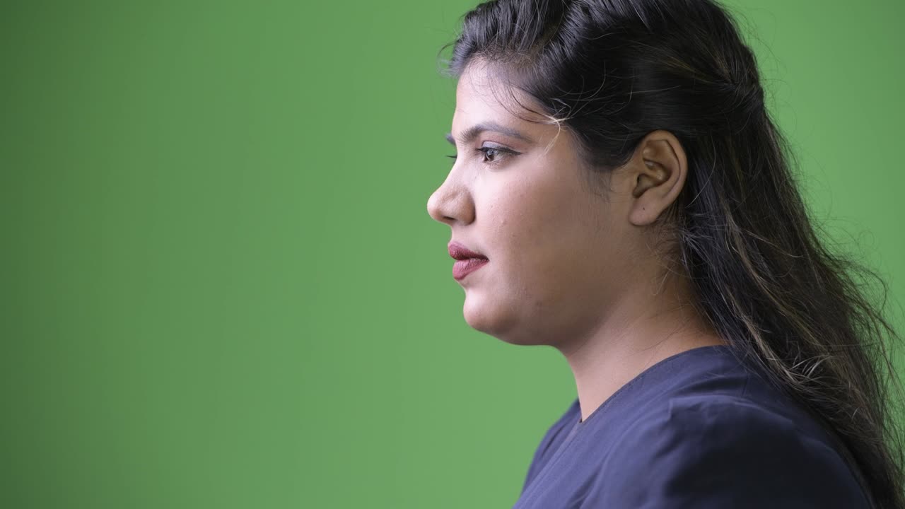 Young overweight beautiful Indian businesswoman against green background