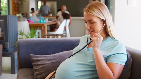 pregnant woman at home listening to baby heartbeat with stethoscope