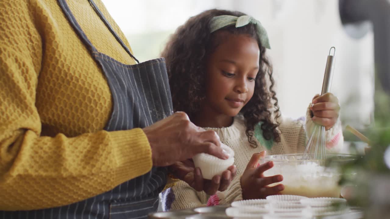 Video of happy african american granddaughter baking with grandmother in kitchen