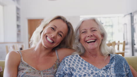 portrait of smiling mother with adult daughter relaxing on sofa at home