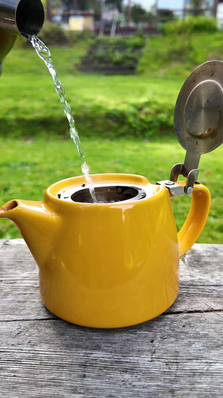 Pouring boiling water into a yellow teapot to brew tea outdoors