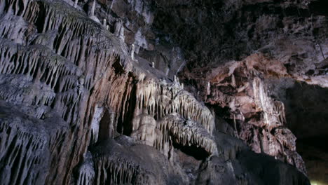 a rugged cave wall features dramatic formations of stalactites and flowstone, illuminated by soft lighting