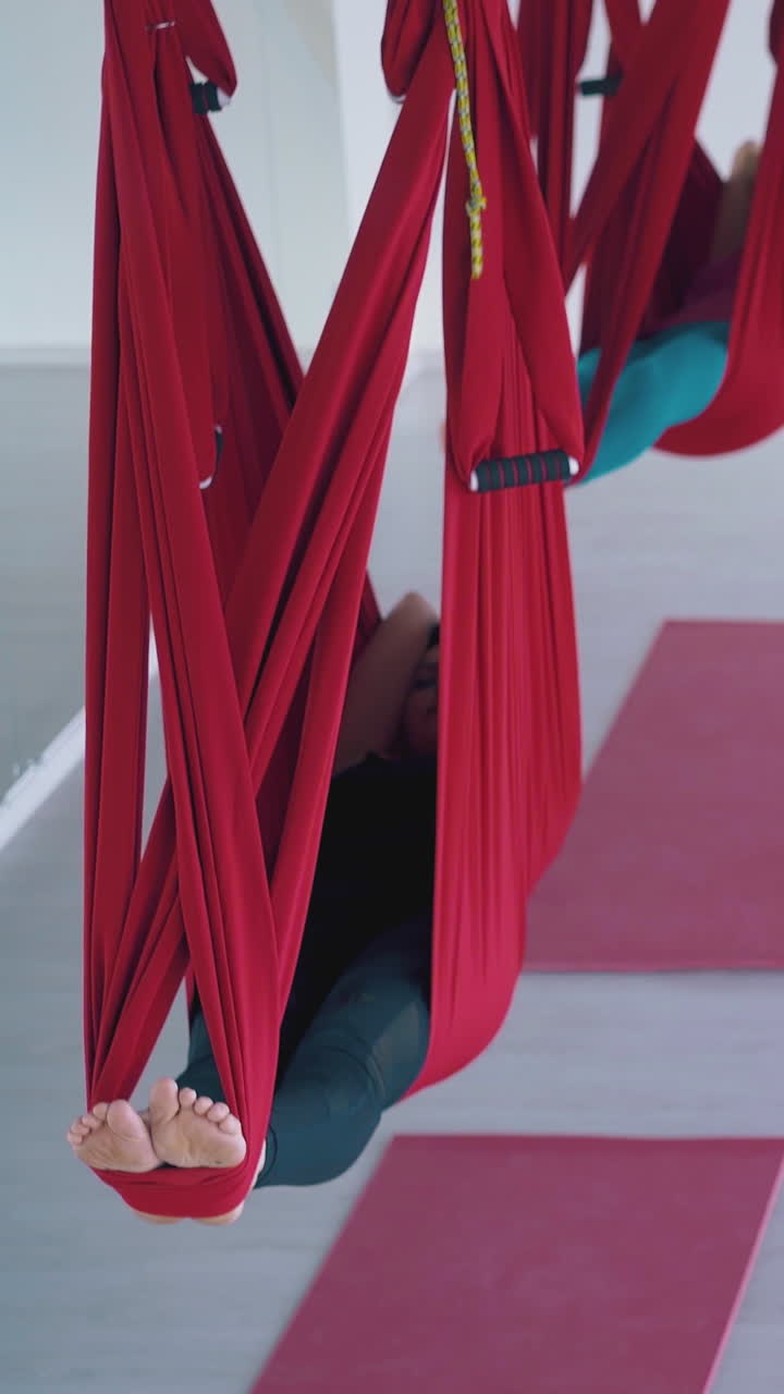 contemporary ladies enjoy lying in red fly yoga hammocks restoring energy after advanced pilates and stretching workout