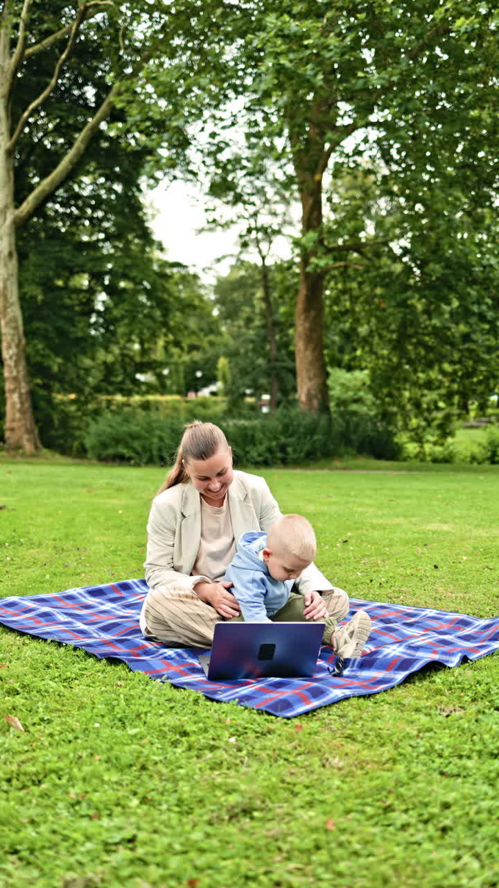 En enlig mor forsøger at arbejde online, mens hun sidder på græsset, mens hendes lille barn leger i nærheden. En mor på barsel arbejder på en bærbar computer, mens hun sidder i parken, mens hendes søn løber i nærheden