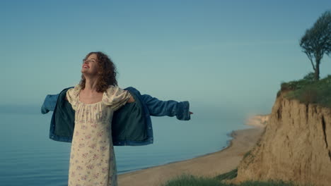 mujer feliz disfrutando de la naturaleza en la playa de arena. niña rizada extendiendo las manos a los lados.