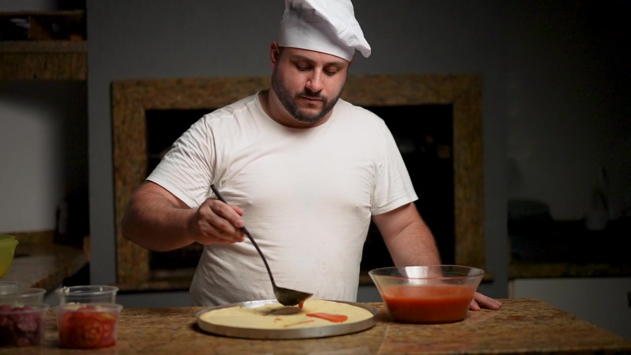 Chef prepara abilmente una base per pizza con un'applicazione liscia di salsa di pomodoro al rallentatore.