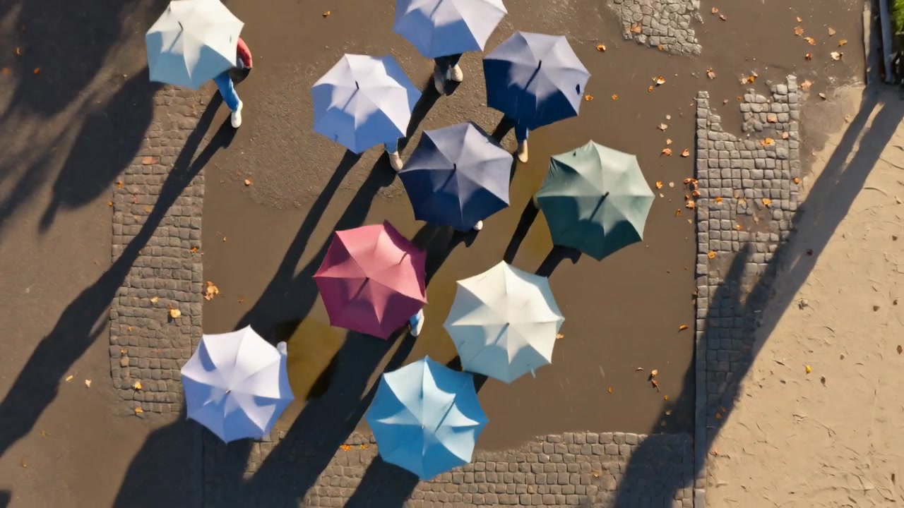 Gruppo di adulti che cammina, indossando cappotti, entra nell'inquadratura muovendosi in gruppo su una piazza con ombrelli colorati.