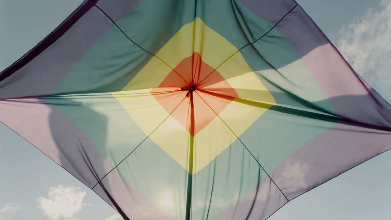 Gennemsigtig, firkantet drage, der blafrer i den blæsende vind og bøjer sig mod den lyse himmel med nav, sprosser og linsereflekser.