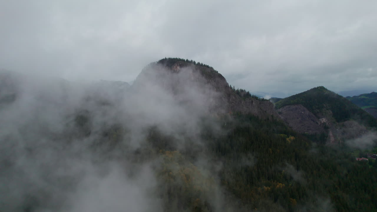Majestic scenery of Lacul Rosu in Romania, featuring a rocky peak surrounded by clouds and forests