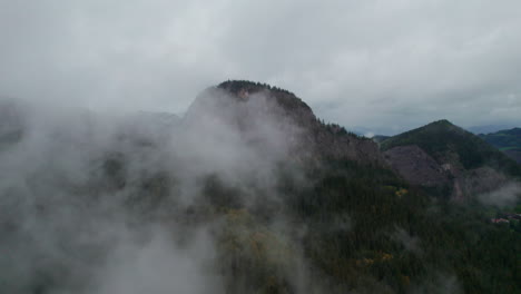 majestic scenery of lacul rosu in romania, featuring a rocky peak surrounded by clouds and forests