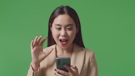 cerca de la mujer de negocios asiática disfruta usando el teléfono móvil y decir wow mientras está de pie en la pantalla verde en el estudio