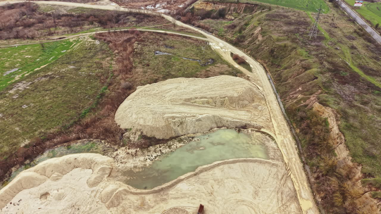 Cantiere edile che mostra attività di movimento terra con macchinari pesanti e specchio d'acqua nelle vicinanze in zona rurale durante il giorno