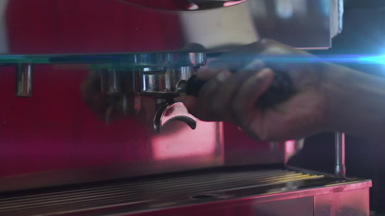 Mão de barista pegando um portafiltro e encaixando em uma máquina de café expresso sob a luz neon para preparar café.