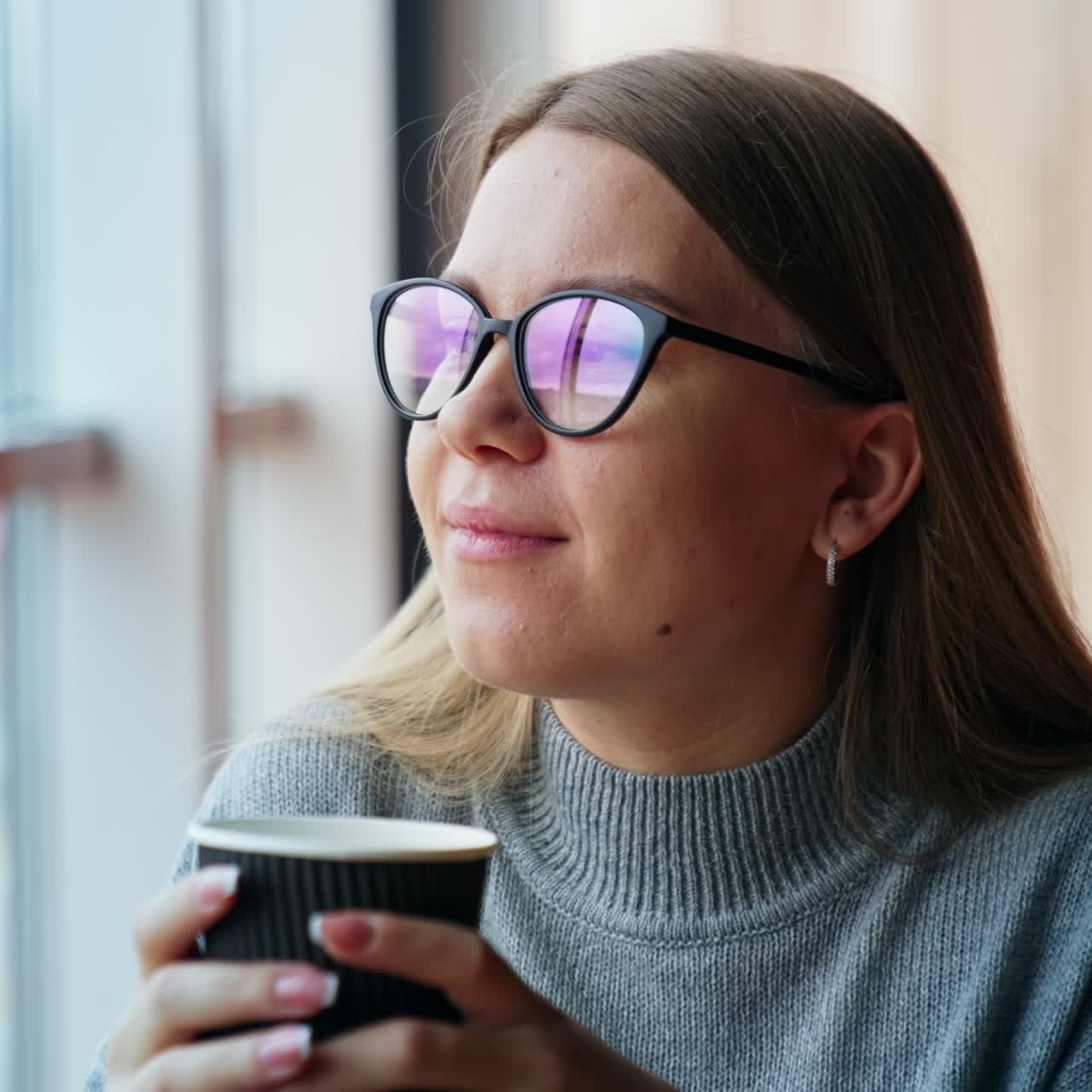 Smiling dreamy lady drinks coffee looking into window. Woman having a break from work at laptop. Lunch time at the working place. Close up