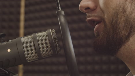 close up of a microphone and a young bearded man's mouth in the recording studio