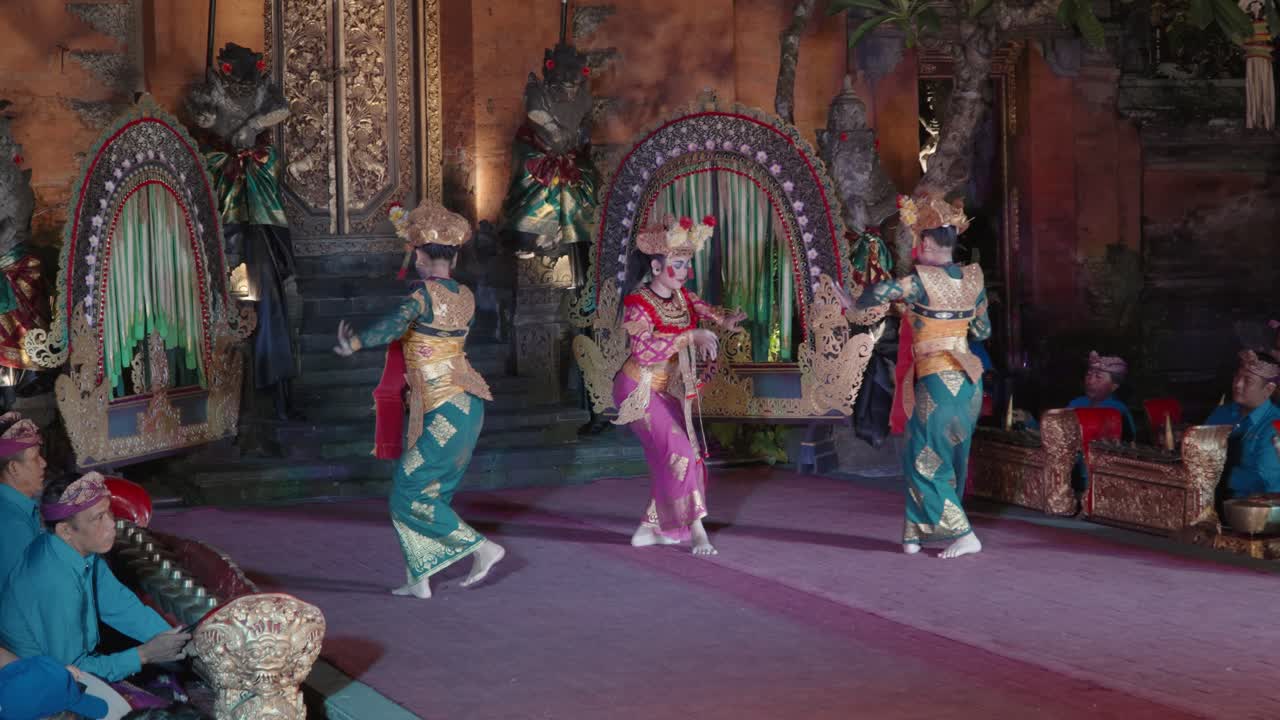 Legong and Ramayana Traditional Theater Dance Night Show at Ubud Palace, Bali - Three Women Dancers with Fans in Colorful Costumes Perform in a Court With Music by Metallophone Orchestra