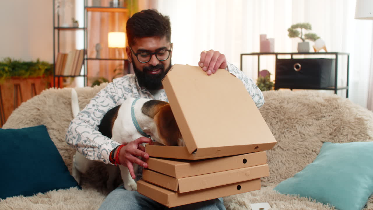 Indian man orders food on smartphone while beagle dog waits and eats from delivered pizza box