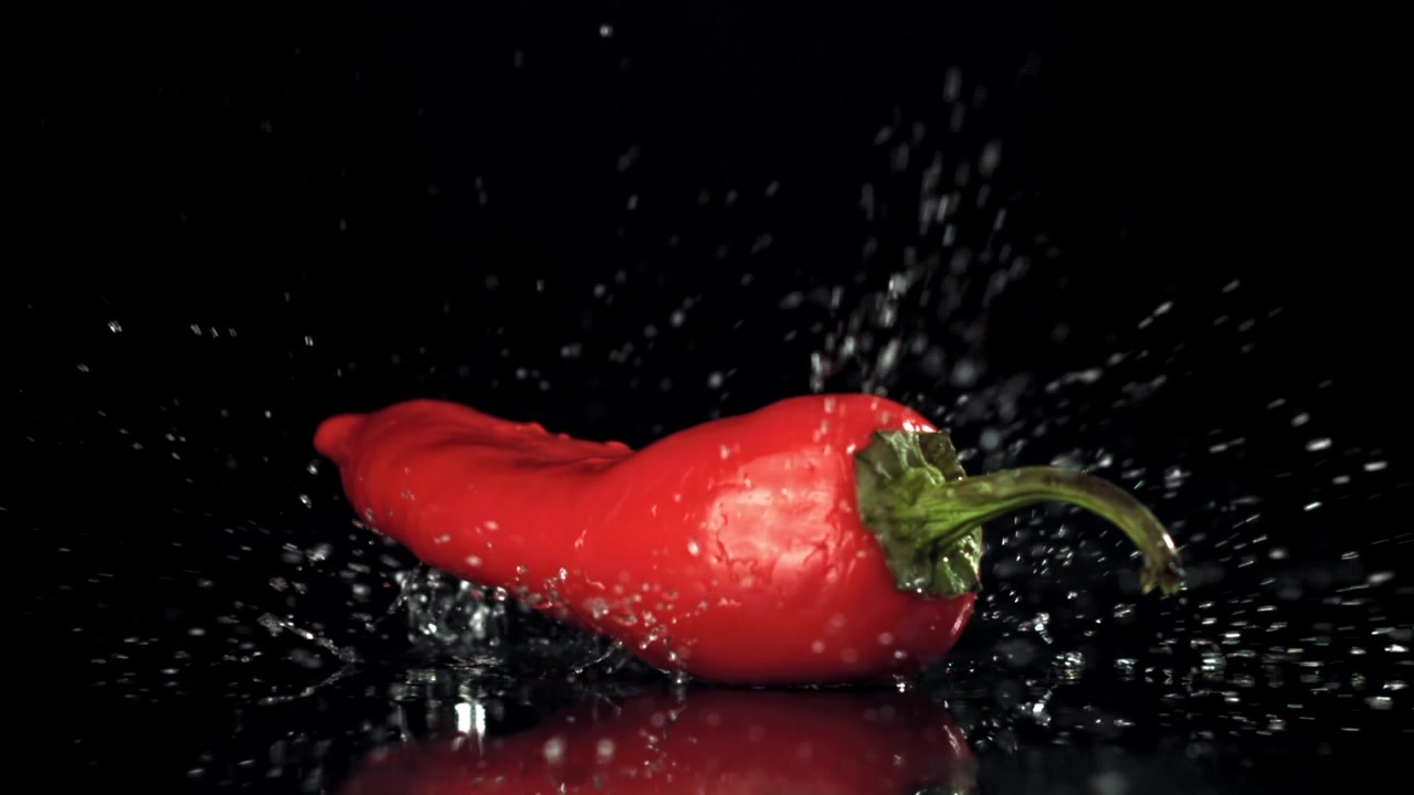 Červená chilli paprička padá a rozstřikuje vodu na černém pozadí.
