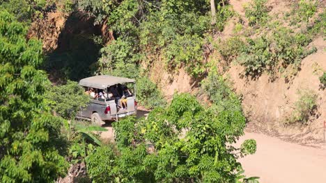 A passenger truck travels along a winding dirt road surrounded by lush greenery in Phang Nga, Thailand, under bright daylight