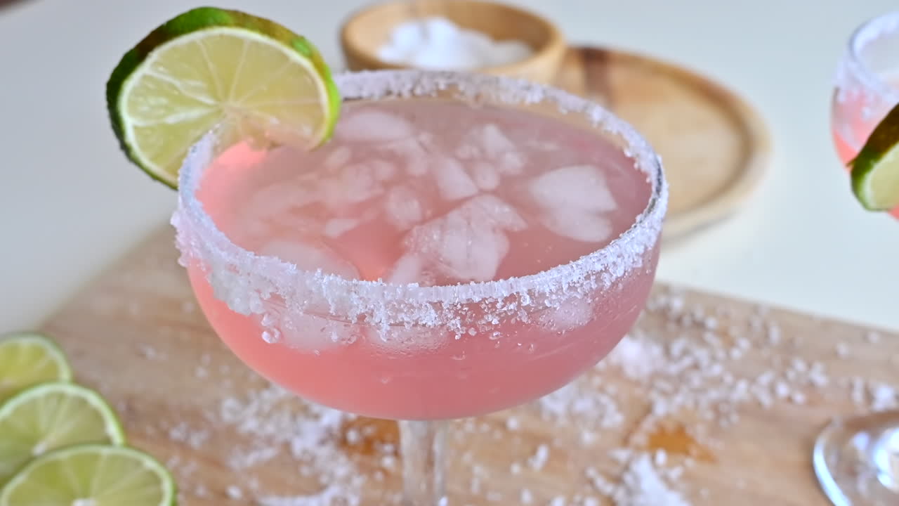Primer plano de un cóctel rosa claro con hielo y rodajas de lima