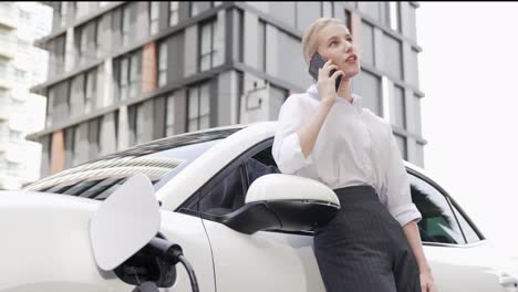 une femme d'affaires progressiste s'appuie sur une voiture électrique et une station de recharge.