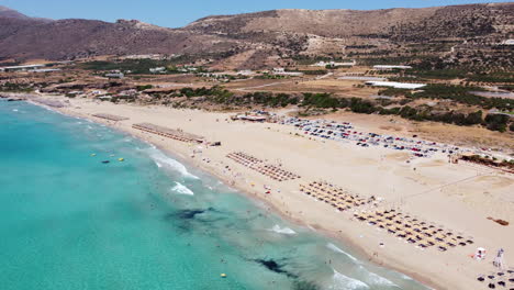 Aerial-view-over-turquoise-waters-and-Umbrellas-in-Falassarna-Beach,-Crete