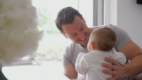 Loving-Father-Holding-3-Month-Old-Baby-Daughter-In-Kitchen-At-Home-Playing-Game