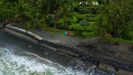 drone pulls back from two women at a small beachfront resort in costa rica. ocean waves crash nearby