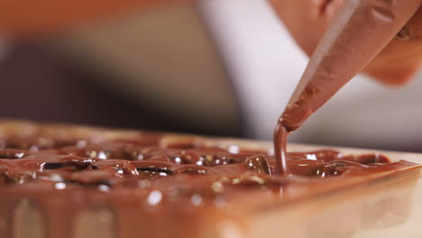 chocolatier squeezing chocolate into praline mold, handmade fine chocolate praline production, close up