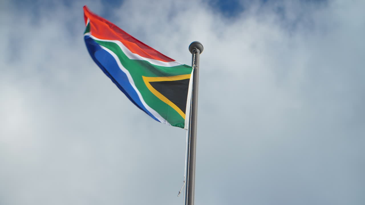 South African flag waving on pole against clouded sky on bright sunny day in center of frame