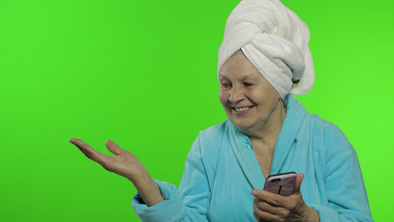 Anziana nonna in accappatoio. Anziana donna con smartphone che indica qualcosa