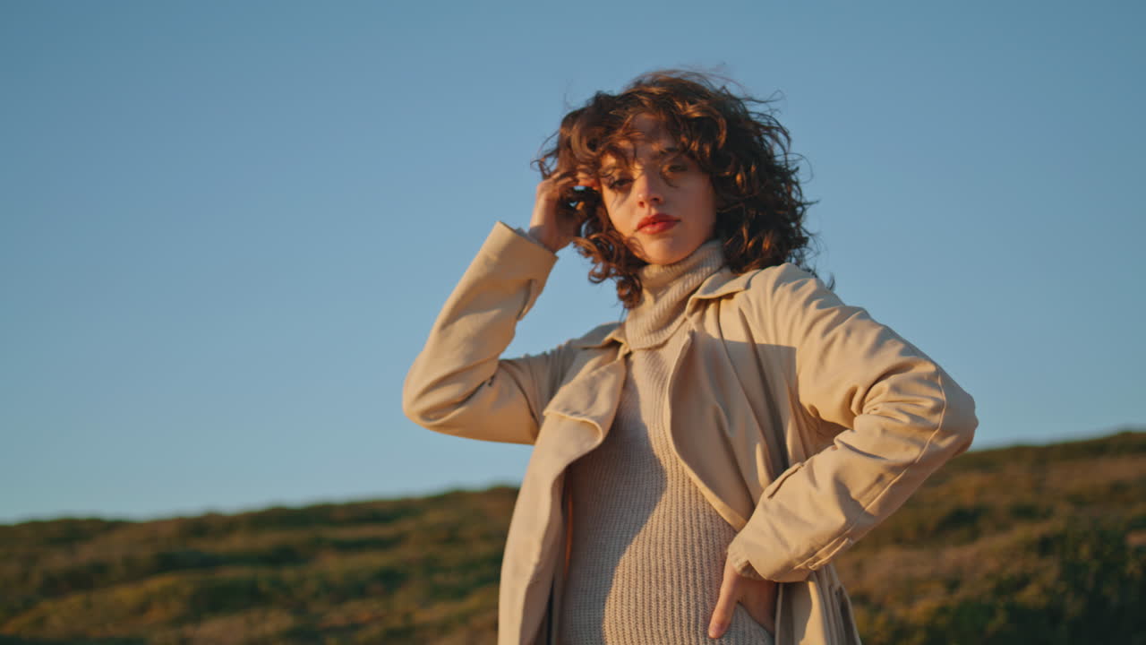 una chica casual posando a la luz del sol de la noche en la orilla del mar. una mujer muy sonriente toca el cabello