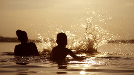 mother throws up her sons into water at sunset. silhouette of a woman and two children having fun together in the river in the evening.