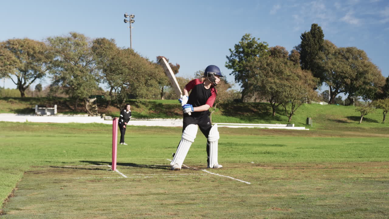 Playing cricket, female batter hitting ball on field during match
