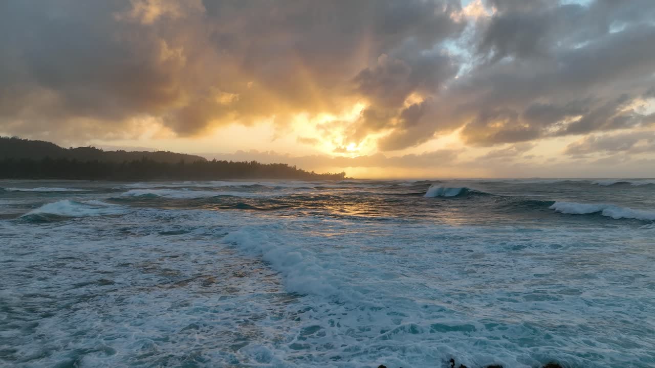 la luz dorada del sol baña el paisaje hawaiano mientras un dron aéreo captura la danza rítmica de las grandes olas del océano durante la puesta del sol.