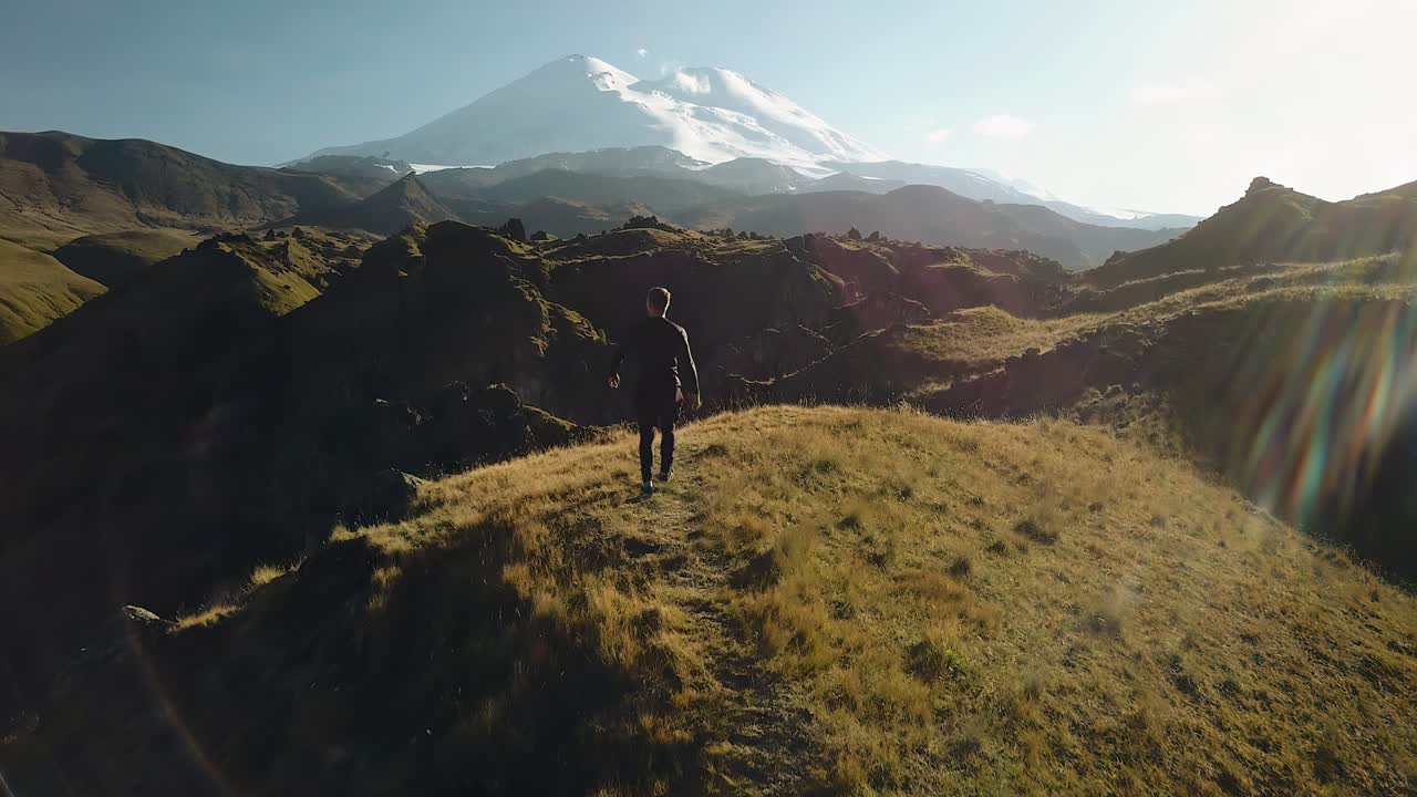 el tipo subió a la montaña en un día soleado. él completa el ascenso. disparando por detrás en movimiento desde el aire