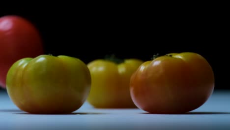 red tomato falling down onto three yellow beefsteak tomatoes with a black background on a white surface