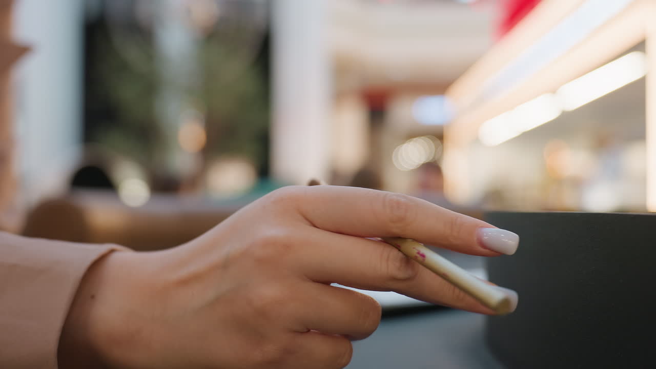 primer plano de unas manos sujetando un pincel con luces bokeh de cafetería, herramientas de maquillaje en la barra, pequeños toques suaves en una taza de cerámica, mezcla de productos con cuidado, movimiento deliberado y concentrado que transmite una preparación tranquila