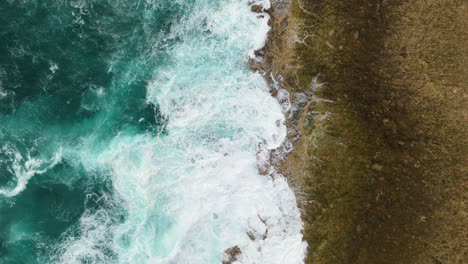 Static-top-down-overview-of-green-ocean-water-and-whitewash-crashing-on-jagged-sharp-rocks