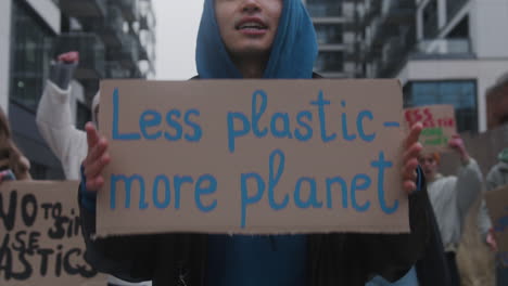 close up of a young male activist holding a cardboard placard against the use of plastic during a climate change protest