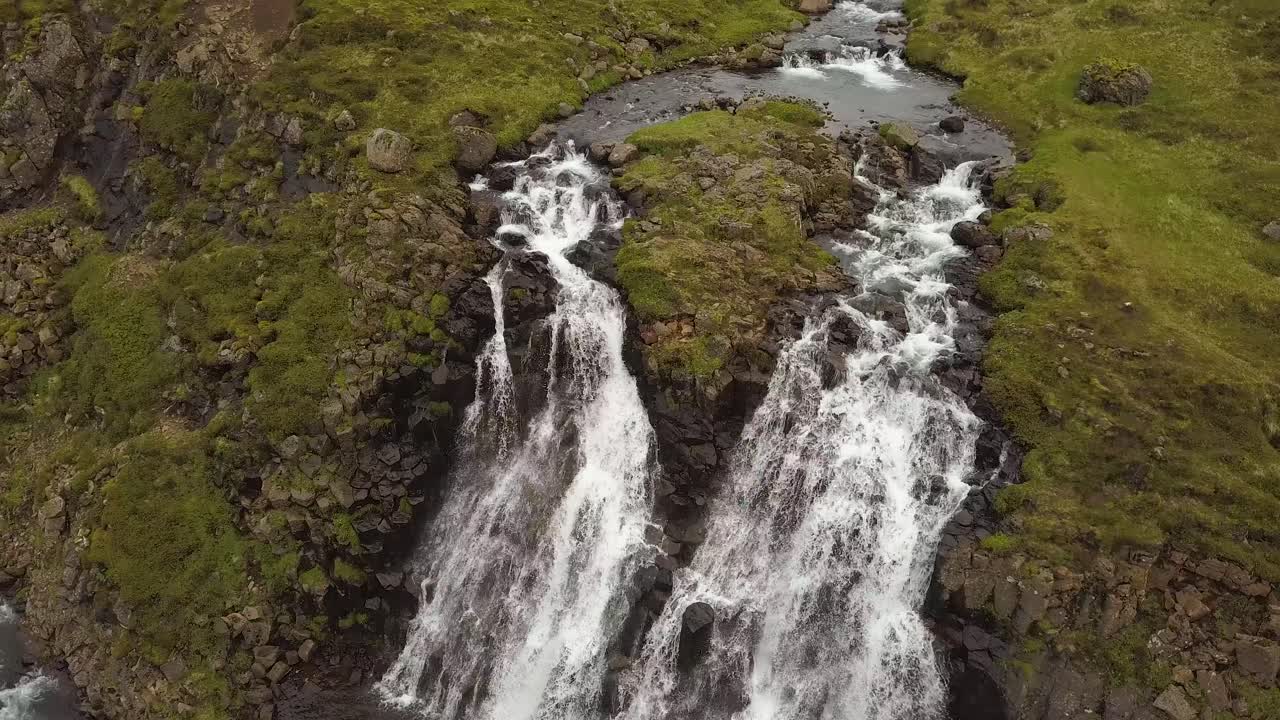 antena que se eleva sobre las cascadas de glymur y el río que fluye por un acantilado rocoso rodeado de montañas verdes durante el día, islandia