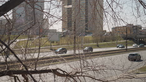 close view of an urban road with cars driving in the background, leafless tree branches in the foreground create a natural frame for the cityscape