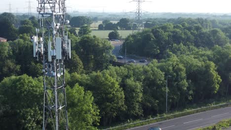 antena de torre de transmisión 5g en el campo británico con vehículos que viajan en el fondo de la carretera vista aérea ascendente lenta