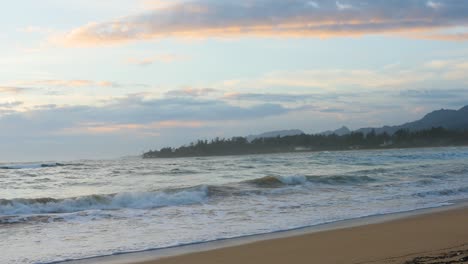 hand held view of a sunset on a hawaii beach on north shore hawaii with pink orange clouds and tropical forest on a peninsula in the background