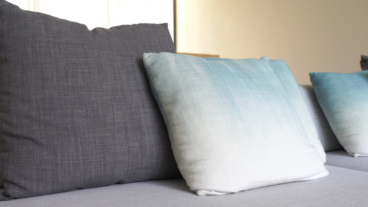 Pan across a grey overstuffed love seat topped with decorative ombre pillows.