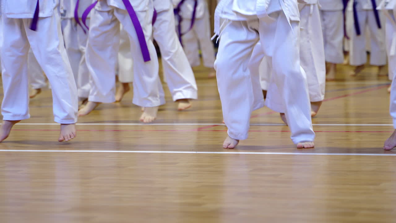 Little sportsmen's bare feet jump on the wooden floor. Athletes in white kimonos warming-up.