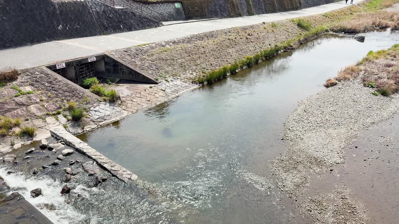 Toma cenital estática de agua cristalina de río fluyendo junto a un terraplén de piedra en Kioto.