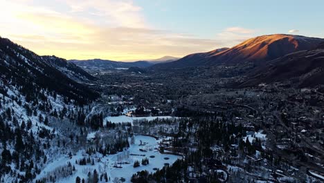 misty mountains and snowy forest bathed in orange-pink sunset glow from alpine drone aerial dolly