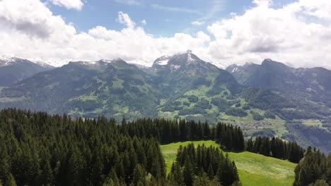 aerial view of amden in the glarus region of switzerland, showing a forested alpine landscape with rolling meadows, mountain peaks, and a solitary cabin under a blue sky